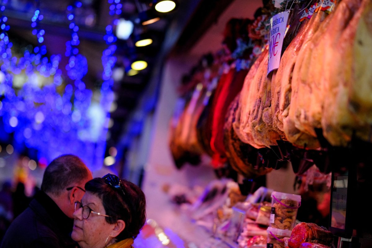 <p>Personas compran comida frente a un Jamón de Bellota colgado en un Mercado de Abastos en Barcelona. (Foto: Reuters)</p>
