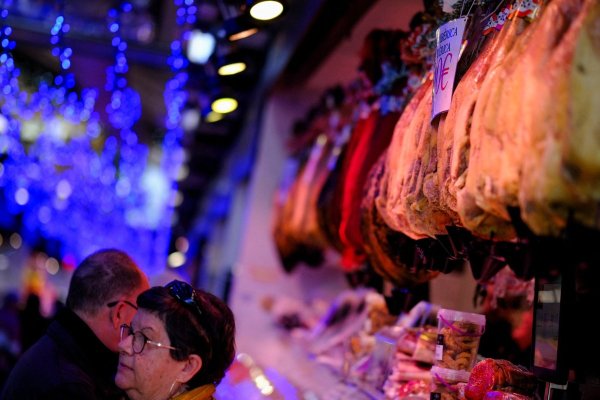 <p>Personas compran comida frente a un Jamón de Bellota colgado en un Mercado de Abastos en Barcelona. (Foto: Reuters)</p>
